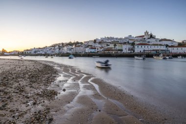 Kumsala bakan bir gün doğumu ve alçak gelgitte liman. Günbatımında Ferragudo, Portimo, Algarve, Portekiz 'de tarihi bir kasabanın panoramik manzarası
