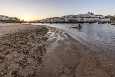 Kumsala bakan bir gün doğumu ve alçak gelgitte liman. Günbatımında Ferragudo, Portimo, Algarve, Portekiz 'de tarihi bir kasabanın panoramik manzarası