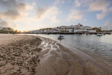 Kumsala bakan bir gün doğumu ve alçak gelgitte liman. Günbatımında Ferragudo, Portimo, Algarve, Portekiz 'de tarihi bir kasabanın panoramik manzarası