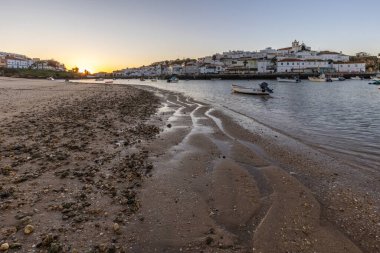 Kumsala bakan bir gün doğumu ve alçak gelgitte liman. Günbatımında Ferragudo, Portimo, Algarve, Portekiz 'de tarihi bir kasabanın panoramik manzarası