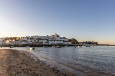 Kumsala bakan bir gün doğumu ve alçak gelgitte liman. Günbatımında Ferragudo, Portimo, Algarve, Portekiz 'de tarihi bir kasabanın panoramik manzarası
