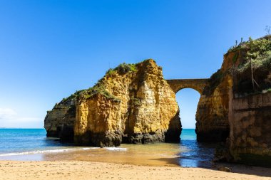 Kumsaldaki sarı kayalar ve uçurumlar. Eski Pinhao Fort Köprüsü 'nün iki uçurumu birleştirdiği deniz kenarında bir koy. Praia da Caldeira plajı, Lagos. Algarve, Portekiz