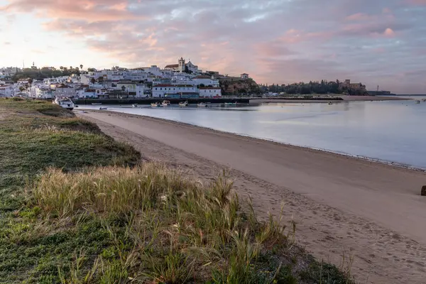 Güneşin doğuşu çayıra, kumlu plaja ve alçak gelgitte limana bakıyor. Sabahın köründe Ferragudo, Portimo, Algarve, Portekiz 'de tarihi bir kasabanın panoramik görüntüsü.