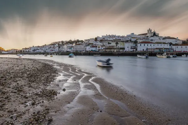 Kumsala bakan bir gün doğumu ve alçak gelgitte liman. Günbatımında Ferragudo, Portimo, Algarve, Portekiz 'de tarihi bir kasabanın panoramik manzarası