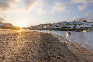 Atlantik Okyanusu 'nda gün doğumu, limanın arkasındaki balıkçı köyünün silueti. Sabah alacakaranlıkta kumsalda. Ferragudo, Portimo, Algarve, Portekiz 'de manzara çekimi