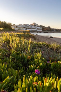 Güneşin doğuşu çayıra, kumlu plaja ve alçak gelgitte limana bakıyor. Günbatımında Ferragudo, Portimo, Algarve, Portekiz 'de tarihi bir kasabanın panoramik manzarası