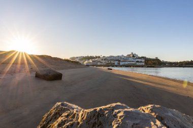 Atlantik Okyanusu 'nda gün doğumu, limanın arkasındaki balıkçı köyünün silueti. Sabah alacakaranlıkta kumsalda. Ferragudo, Portimo, Algarve, Portekiz 'de manzara çekimi