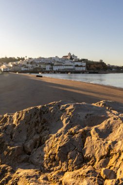 Atlantik Okyanusu 'nda gün doğumu, limanın arkasındaki balıkçı köyünün silueti. Sabah alacakaranlıkta kumsalda. Ferragudo, Portimo, Algarve, Portekiz 'de manzara çekimi