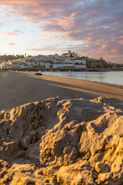 Atlantik Okyanusu 'nda gün doğumu, limanın arkasındaki balıkçı köyünün silueti. Sabah alacakaranlıkta kumsalda. Ferragudo, Portimo, Algarve, Portekiz 'de manzara çekimi