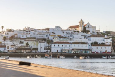 Atlantik Okyanusu 'nda gün doğumu, limanın arkasındaki balıkçı köyünün silueti. Sabah alacakaranlıkta kumsalda. Ferragudo, Portimo, Algarve, Portekiz 'de manzara çekimi
