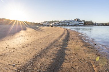 Atlantik Okyanusu 'nda gün doğumu, limanın arkasındaki balıkçı köyünün silueti. Sabah alacakaranlıkta kumsalda. Ferragudo, Portimo, Algarve, Portekiz 'de manzara çekimi