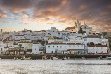 Atlantik Okyanusu 'nda gün doğumu, limanın arkasındaki balıkçı köyünün silueti. Sabah alacakaranlıkta kumsalda. Ferragudo, Portimo, Algarve, Portekiz 'de manzara çekimi