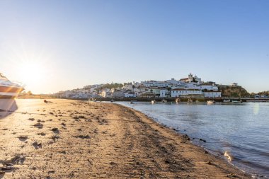 Atlantik Okyanusu 'nda gün doğumu, limanın arkasındaki balıkçı köyünün silueti. Sabah alacakaranlıkta kumsalda. Ferragudo, Portimo, Algarve, Portekiz 'de manzara çekimi