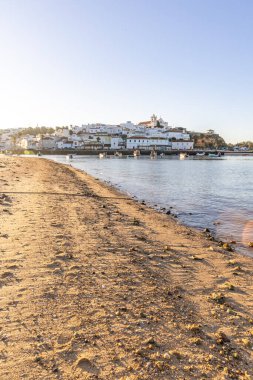 Atlantik Okyanusu 'nda gün doğumu, limanın arkasındaki balıkçı köyünün silueti. Sabah alacakaranlıkta kumsalda. Ferragudo, Portimo, Algarve, Portekiz 'de manzara çekimi