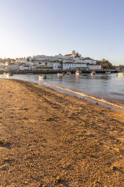Atlantik Okyanusu 'nda gün doğumu, limanın arkasındaki balıkçı köyünün silueti. Sabah alacakaranlıkta kumsalda. Ferragudo, Portimo, Algarve, Portekiz 'de manzara çekimi