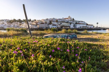 Güneşin doğuşu çayıra, kumlu plaja ve alçak gelgitte limana bakıyor. Günbatımında Ferragudo, Portimo, Algarve, Portekiz 'de tarihi bir kasabanın panoramik manzarası