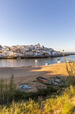 Güneşin doğuşu çayıra, kumlu plaja ve alçak gelgitte limana bakıyor. Günbatımında Ferragudo, Portimo, Algarve, Portekiz 'de tarihi bir kasabanın panoramik manzarası