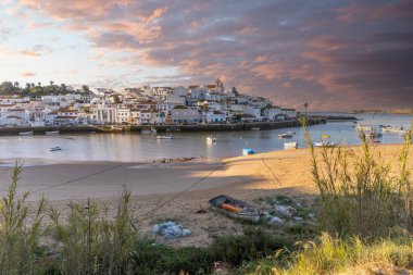 Güneşin doğuşu çayıra, kumlu plaja ve alçak gelgitte limana bakıyor. Günbatımında Ferragudo, Portimo, Algarve, Portekiz 'de tarihi bir kasabanın panoramik manzarası