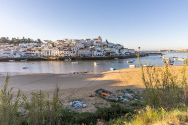 Güneşin doğuşu çayıra, kumlu plaja ve alçak gelgitte limana bakıyor. Günbatımında Ferragudo, Portimo, Algarve, Portekiz 'de tarihi bir kasabanın panoramik manzarası