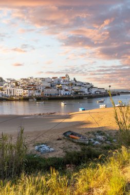 Güneşin doğuşu çayıra, kumlu plaja ve alçak gelgitte limana bakıyor. Günbatımında Ferragudo, Portimo, Algarve, Portekiz 'de tarihi bir kasabanın panoramik manzarası