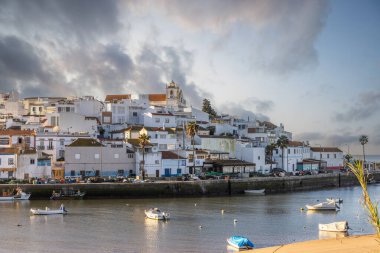 Atlantik Okyanusu 'nda gün doğumu, limanın arkasındaki balıkçı köyünün silueti. Sabah alacakaranlıkta kumsalda. Ferragudo, Portimo, Algarve, Portekiz 'de manzara çekimi