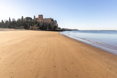 Atlantik 'te gün doğumu, sahilin ortasında bir kale. Limanı koruyan tarihi bir bina. Castelo de Ferragudo, kumlu Praia da Angrinha sahilinde, Portimo, Algarve, Portekiz