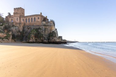 Atlantik 'te gün doğumu, sahilin ortasında bir kale. Limanı koruyan tarihi bir bina. Castelo de Ferragudo, kumlu Praia da Angrinha sahilinde, Portimo, Algarve, Portekiz