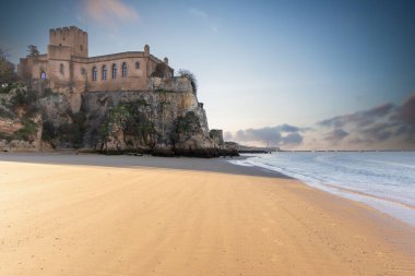 Atlantik 'te gün doğumu, sahilin ortasında bir kale. Limanı koruyan tarihi bir bina. Castelo de Ferragudo, kumlu Praia da Angrinha sahilinde, Portimo, Algarve, Portekiz