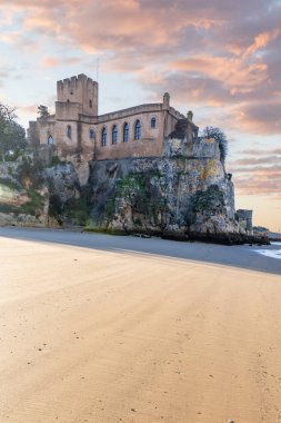 Atlantik 'te gün doğumu, sahilin ortasında bir kale. Limanı koruyan tarihi bir bina. Castelo de Ferragudo, kumlu Praia da Angrinha sahilinde, Portimo, Algarve, Portekiz