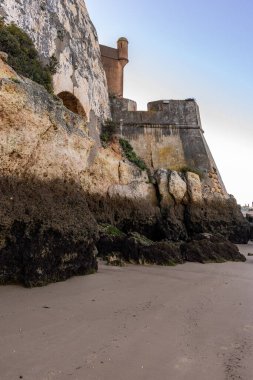 Atlantik 'te gün doğumu, sahilin ortasında bir kale. Limanı koruyan tarihi bir bina. Castelo de Ferragudo, kumlu Praia da Angrinha sahilinde, Portimo, Algarve, Portekiz