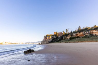 Atlantik 'te gün doğumu, sahilin ortasında bir kale. Limanı koruyan tarihi bir bina. Castelo de Ferragudo, kumlu Praia da Angrinha sahilinde, Portimo, Algarve, Portekiz