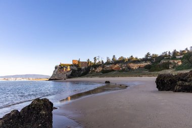 Atlantik 'te gün doğumu, sahilin ortasında bir kale. Limanı koruyan tarihi bir bina. Castelo de Ferragudo, kumlu Praia da Angrinha sahilinde, Portimo, Algarve, Portekiz