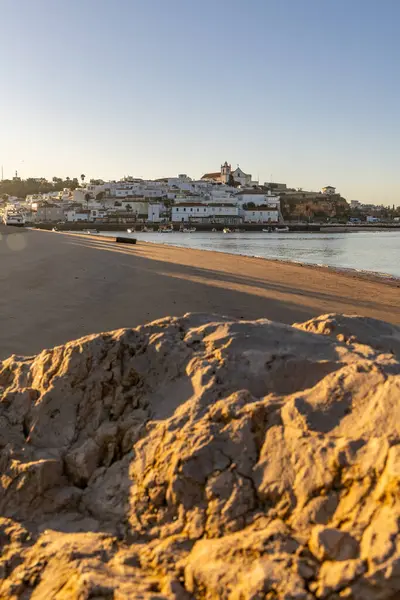 Atlantik Okyanusu 'nda gün doğumu, limanın arkasındaki balıkçı köyünün silueti. Sabah alacakaranlıkta kumsalda. Ferragudo, Portimo, Algarve, Portekiz 'de manzara çekimi