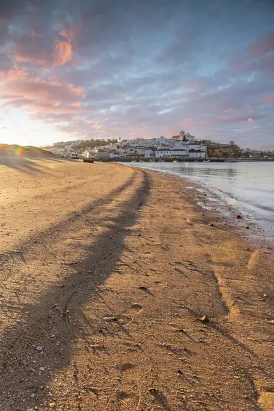 Atlantik Okyanusu 'nda gün doğumu, limanın arkasındaki balıkçı köyünün silueti. Sabah alacakaranlıkta kumsalda. Ferragudo, Portimo, Algarve, Portekiz 'de manzara çekimi