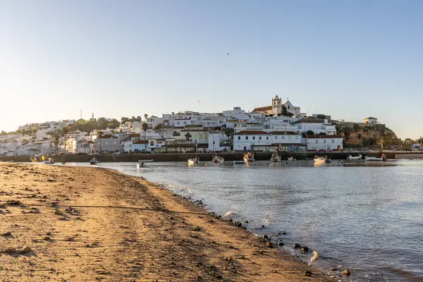 Atlantik Okyanusu 'nda gün doğumu, limanın arkasındaki balıkçı köyünün silueti. Sabah alacakaranlıkta kumsalda. Ferragudo, Portimo, Algarve, Portekiz 'de manzara çekimi