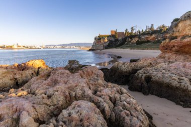 Atlantik 'te gün doğumu, sahilin ortasında bir kale. Limanı koruyan tarihi bir bina. Castelo de Ferragudo, kumlu Praia da Angrinha sahilinde, Portimo, Algarve, Portekiz