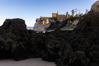 Atlantik 'te gün doğumu, sahilin ortasında bir kale. Limanı koruyan tarihi bir bina. Castelo de Ferragudo, kumlu Praia da Angrinha sahilinde, Portimo, Algarve, Portekiz