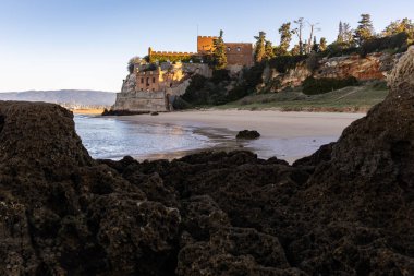 Atlantik 'te gün doğumu, sahilin ortasında bir kale. Limanı koruyan tarihi bir bina. Castelo de Ferragudo, kumlu Praia da Angrinha sahilinde, Portimo, Algarve, Portekiz