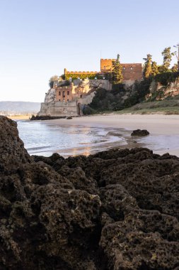 Atlantik 'te gün doğumu, sahilin ortasında bir kale. Limanı koruyan tarihi bir bina. Castelo de Ferragudo, kumlu Praia da Angrinha sahilinde, Portimo, Algarve, Portekiz
