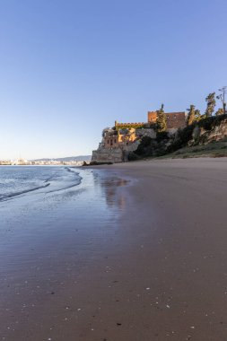 Atlantik 'te gün doğumu, sahilin ortasında bir kale. Limanı koruyan tarihi bir bina. Castelo de Ferragudo, kumlu Praia da Angrinha sahilinde, Portimo, Algarve, Portekiz