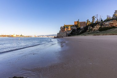 Atlantik 'te gün doğumu, sahilin ortasında bir kale. Limanı koruyan tarihi bir bina. Castelo de Ferragudo, kumlu Praia da Angrinha sahilinde, Portimo, Algarve, Portekiz