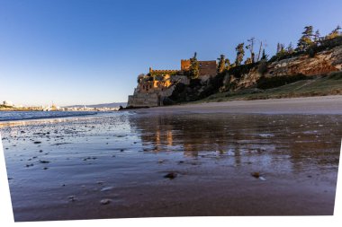 Atlantik 'te gün doğumu, sahilin ortasında bir kale. Limanı koruyan tarihi bir bina. Castelo de Ferragudo, kumlu Praia da Angrinha sahilinde, Portimo, Algarve, Portekiz