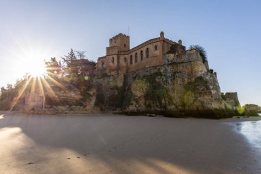 Atlantik 'te gün doğumu, sahilin ortasında bir kale. Limanı koruyan tarihi bir bina. Castelo de Ferragudo, kumlu Praia da Angrinha sahilinde, Portimo, Algarve, Portekiz