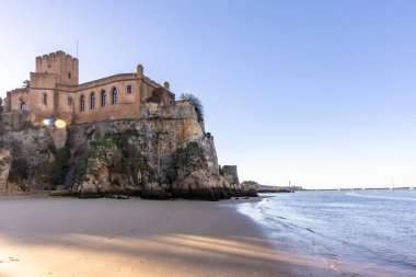 Atlantik 'te gün doğumu, sahilin ortasında bir kale. Limanı koruyan tarihi bir bina. Castelo de Ferragudo, kumlu Praia da Angrinha sahilinde, Portimo, Algarve, Portekiz