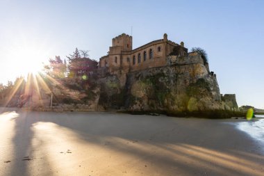 Atlantik 'te gün doğumu, sahilin ortasında bir kale. Limanı koruyan tarihi bir bina. Castelo de Ferragudo, kumlu Praia da Angrinha sahilinde, Portimo, Algarve, Portekiz