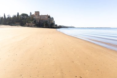Atlantik 'te gün doğumu, sahilin ortasında bir kale. Limanı koruyan tarihi bir bina. Castelo de Ferragudo, kumlu Praia da Angrinha sahilinde, Portimo, Algarve, Portekiz