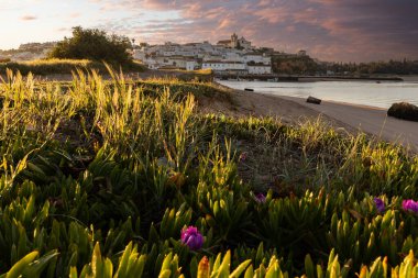 Güneşin doğuşu çayıra, kumlu plaja ve alçak gelgitte limana bakıyor. Günbatımında Ferragudo, Portimo, Algarve, Portekiz 'de tarihi bir kasabanın panoramik manzarası