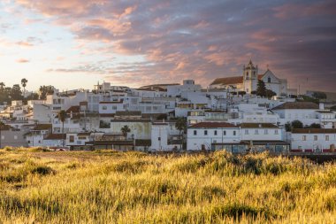 Güneşin doğuşu çayıra, kumlu plaja ve alçak gelgitte limana bakıyor. Günbatımında Ferragudo, Portimo, Algarve, Portekiz 'de tarihi bir kasabanın panoramik manzarası