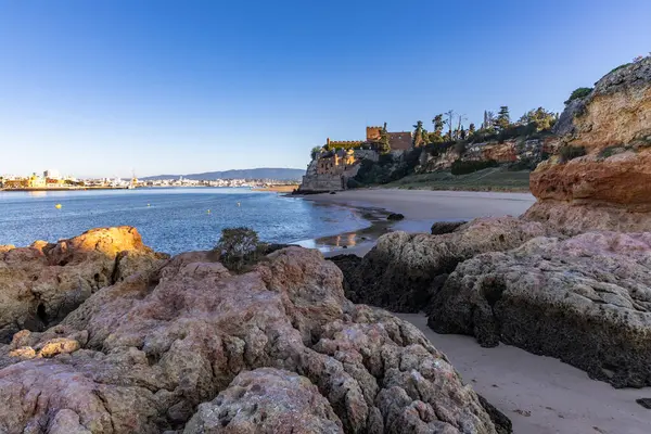 Atlantik 'te gün doğumu, sahilin ortasında bir kale. Limanı koruyan tarihi bir bina. Castelo de Ferragudo, kumlu Praia da Angrinha sahilinde, Portimo, Algarve, Portekiz