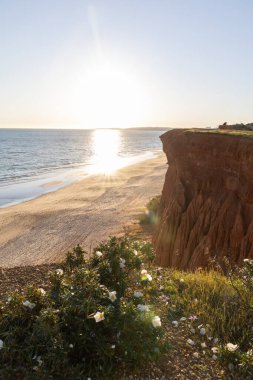 Atlantik 'in sakin sularında, gelgitte yansımaları olan deniz. Praia do Poo Velho, Praia da Falsia, Quarteira, Algarve, Portekiz uçurumlarındaki gün batımının manzarası.